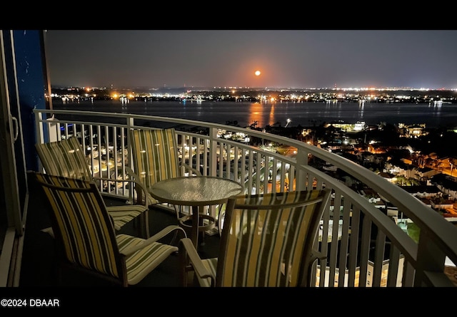 balcony at night featuring a water view