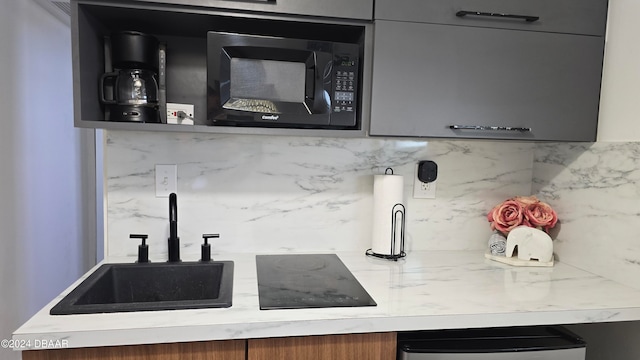 kitchen with light stone countertops, sink, gray cabinets, and tasteful backsplash