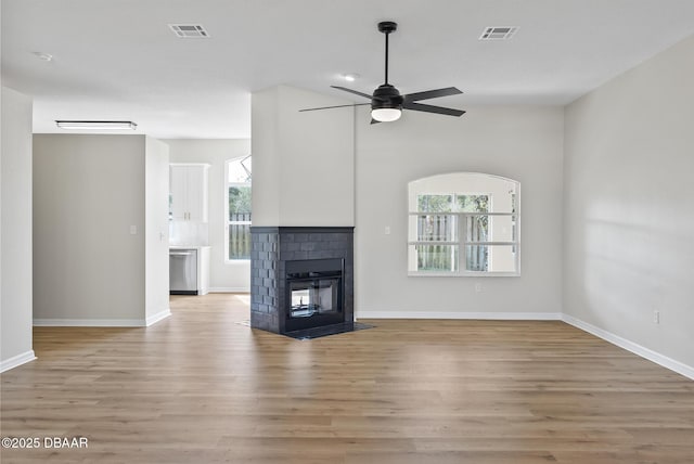 unfurnished living room featuring a multi sided fireplace, ceiling fan, and light wood-type flooring