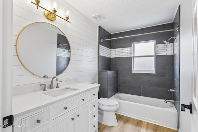 full bathroom with vanity, a textured ceiling, tiled shower / bath combo, toilet, and hardwood / wood-style flooring