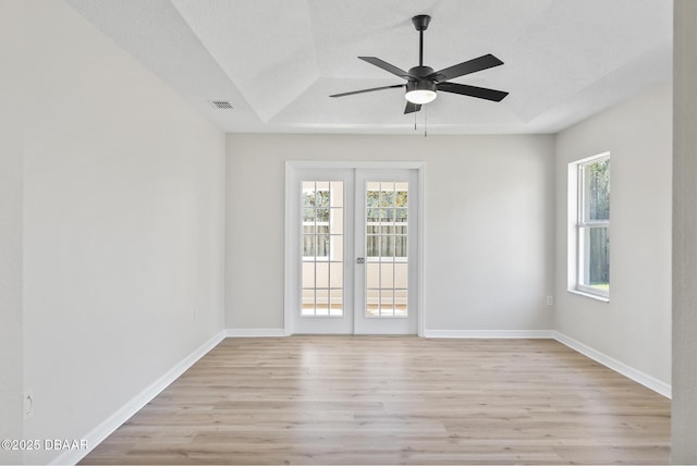 spare room featuring french doors, light hardwood / wood-style floors, a tray ceiling, ceiling fan, and a textured ceiling