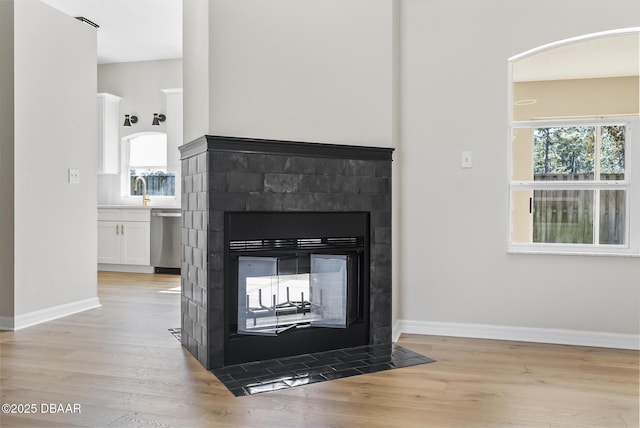 room details with a multi sided fireplace, stainless steel dishwasher, sink, and wood-type flooring