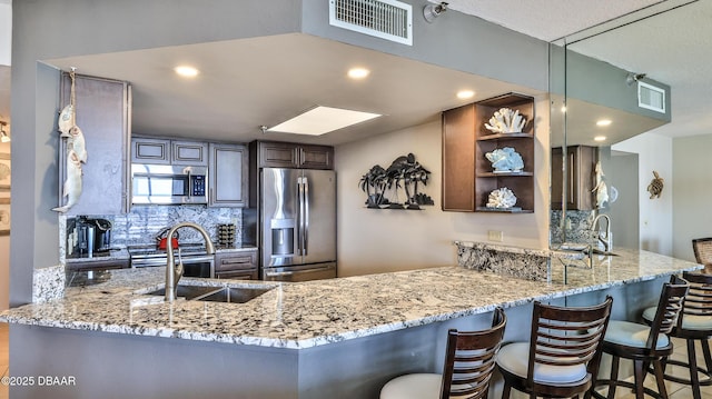 kitchen with tasteful backsplash, sink, a kitchen bar, kitchen peninsula, and stainless steel appliances