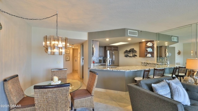 kitchen featuring stainless steel refrigerator with ice dispenser, light stone counters, a textured ceiling, light tile patterned floors, and kitchen peninsula