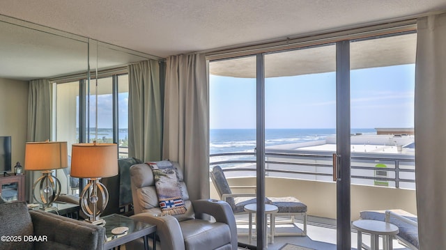 interior space with a water view, floor to ceiling windows, a view of the beach, and a textured ceiling