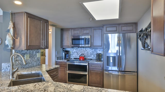 kitchen with light stone counters, stainless steel appliances, sink, and decorative backsplash