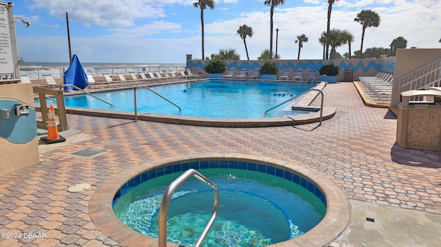 view of swimming pool with a water view, a patio, and a hot tub