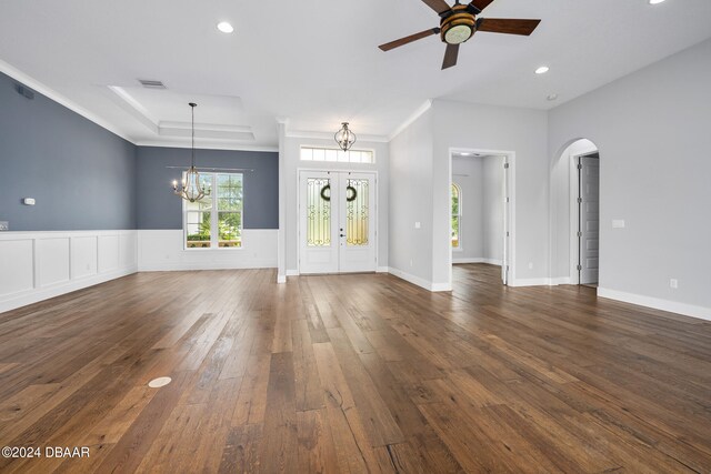 unfurnished living room featuring dark hardwood / wood-style flooring, a tray ceiling, ceiling fan with notable chandelier, and crown molding