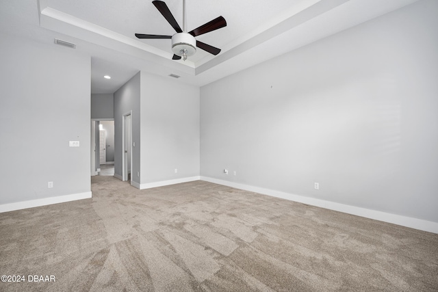 carpeted spare room featuring a tray ceiling and ceiling fan