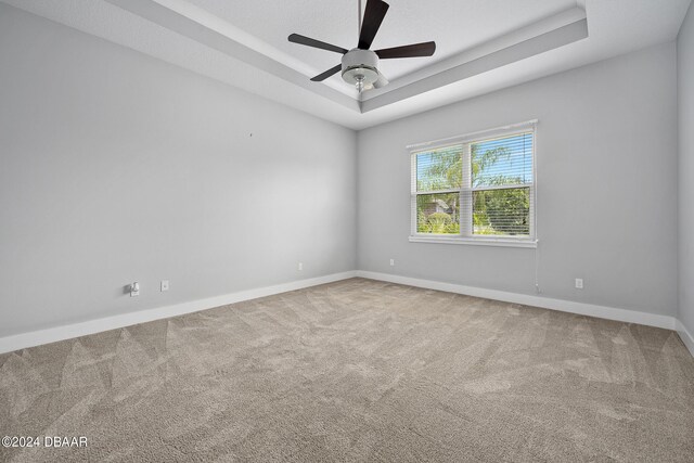 carpeted empty room with ceiling fan and a raised ceiling