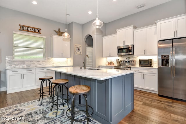 kitchen featuring sink, appliances with stainless steel finishes, decorative light fixtures, an island with sink, and white cabinets