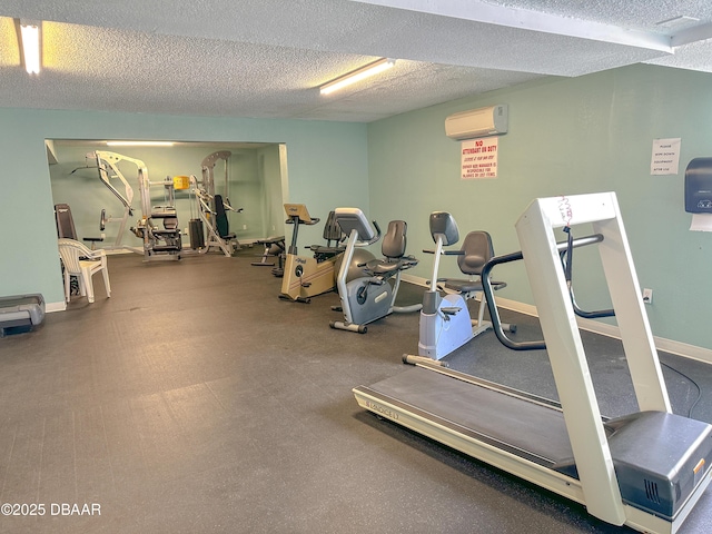 gym featuring a wall unit AC, a textured ceiling, and baseboards