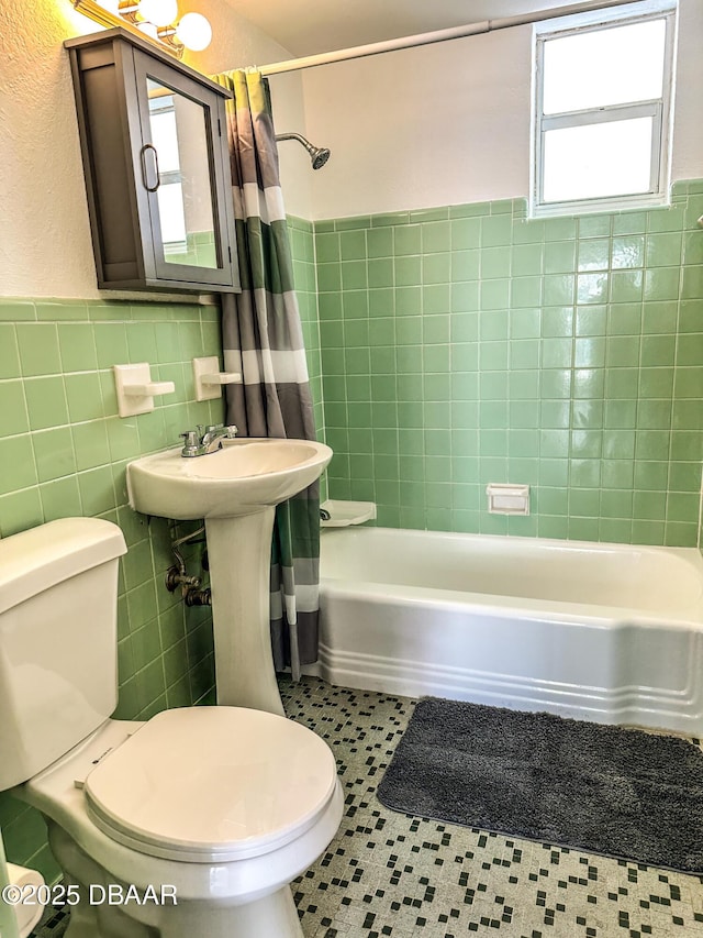 bathroom with toilet, tile walls, wainscoting, tile patterned floors, and shower / bath combo