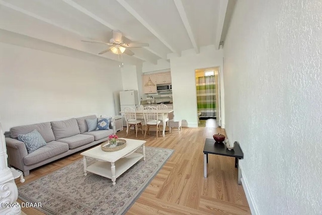 living area with a ceiling fan, light wood-style flooring, beam ceiling, and baseboards