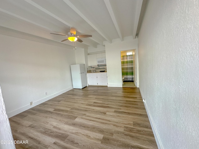 spare room featuring baseboards, a textured wall, ceiling fan, wood finished floors, and beam ceiling