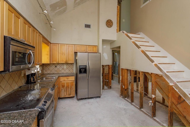 kitchen with decorative backsplash, sink, stainless steel appliances, and a towering ceiling