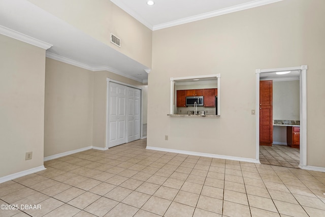 unfurnished living room with ornamental molding, a towering ceiling, light tile patterned floors, and baseboards