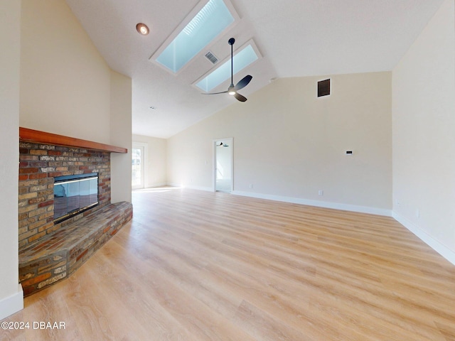 unfurnished living room featuring a fireplace, light hardwood / wood-style flooring, ceiling fan, and vaulted ceiling with skylight