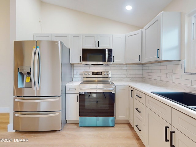 kitchen with backsplash, light hardwood / wood-style flooring, lofted ceiling, and appliances with stainless steel finishes