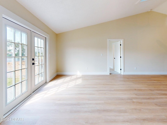 empty room with a healthy amount of sunlight, light hardwood / wood-style flooring, french doors, and lofted ceiling