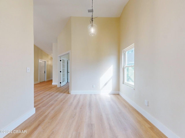 empty room featuring high vaulted ceiling and light hardwood / wood-style floors