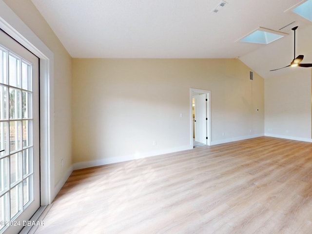 spare room with ceiling fan, vaulted ceiling with skylight, and light wood-type flooring