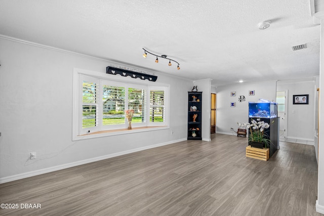 unfurnished living room with baseboards, visible vents, wood finished floors, crown molding, and a textured ceiling