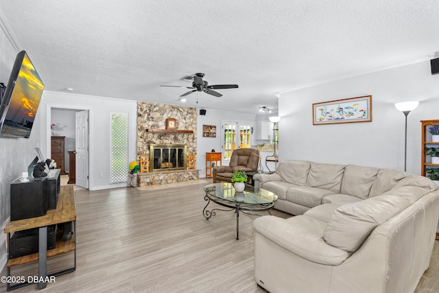 living room featuring a ceiling fan, a fireplace, a textured ceiling, and light wood finished floors