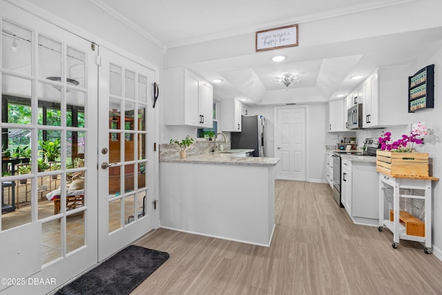 kitchen featuring appliances with stainless steel finishes, crown molding, light wood-type flooring, white cabinetry, and a sink