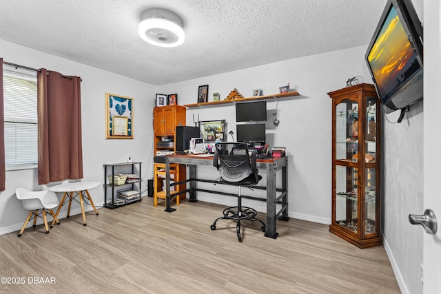 office area with baseboards, light wood-style flooring, and a textured ceiling