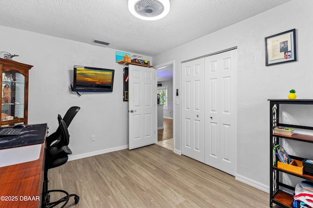 office with baseboards, visible vents, light wood-style flooring, and a textured ceiling