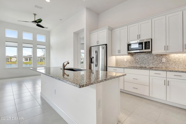 kitchen featuring light tile patterned floors, stainless steel appliances, a kitchen island with sink, white cabinetry, and a sink