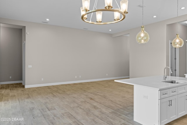 kitchen with baseboards, hanging light fixtures, light countertops, light wood-type flooring, and a sink