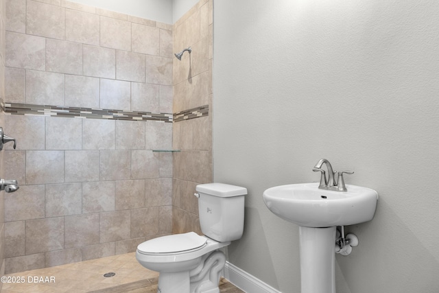 full bath featuring toilet, a sink, baseboards, and tiled shower