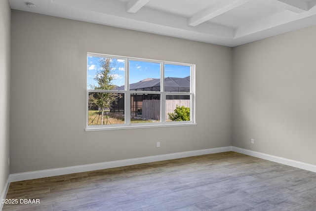 spare room with beam ceiling, baseboards, and wood finished floors