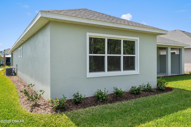 view of side of home featuring stucco siding, roof with shingles, a lawn, and central air condition unit