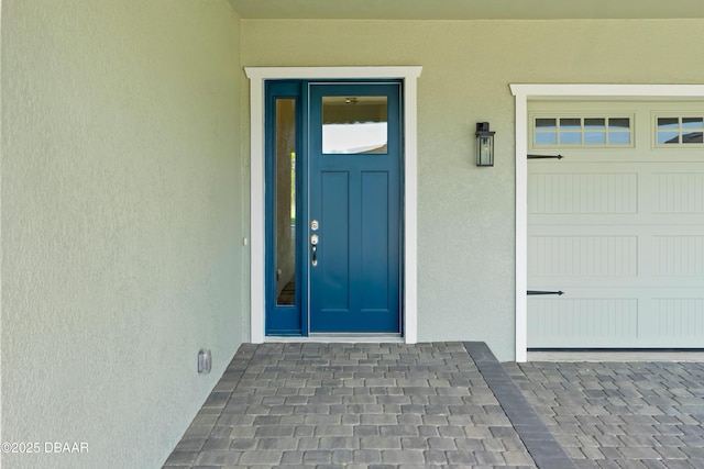 view of exterior entry featuring a garage and stucco siding