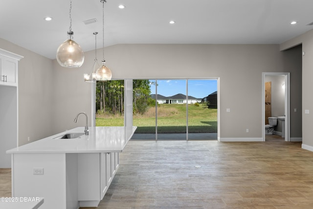 kitchen with light countertops, white cabinets, a sink, an island with sink, and light wood-type flooring