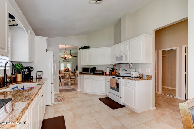 kitchen featuring vaulted ceiling, white cabinets, sink, white appliances, and dark stone countertops