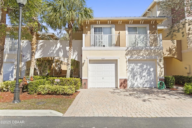 view of front facade with stucco siding, an attached garage, decorative driveway, and a balcony