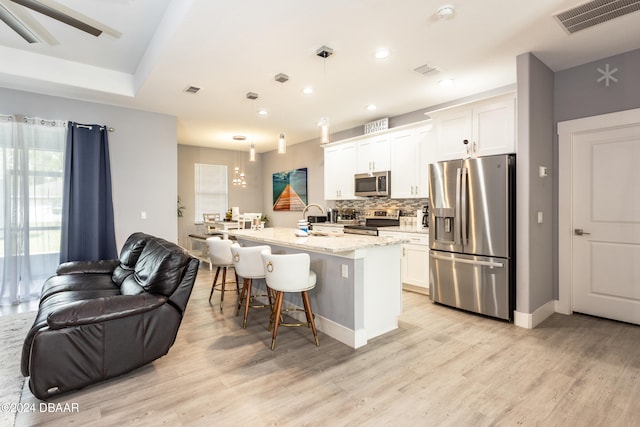 kitchen with white cabinets, stainless steel appliances, decorative light fixtures, and an island with sink