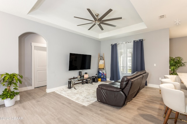 living room with light hardwood / wood-style flooring, ceiling fan, and a tray ceiling