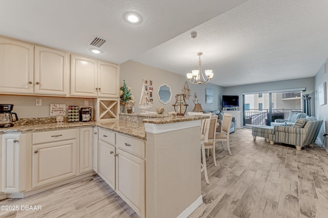 kitchen with hanging light fixtures, light stone countertops, kitchen peninsula, and light wood-type flooring