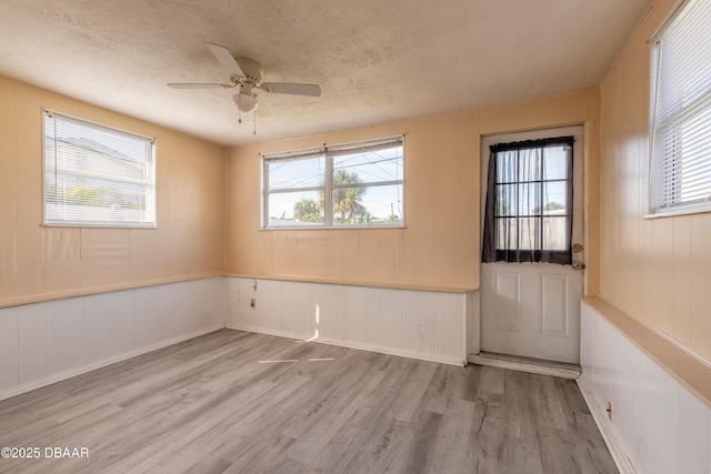 unfurnished room featuring ceiling fan, a textured ceiling, a healthy amount of sunlight, and light wood-type flooring