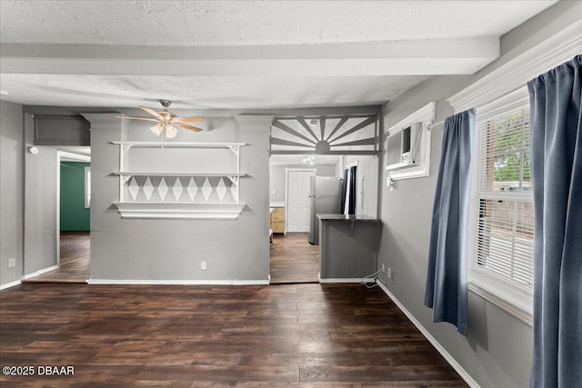 unfurnished living room with ceiling fan, wood finished floors, a wall unit AC, beamed ceiling, and baseboards