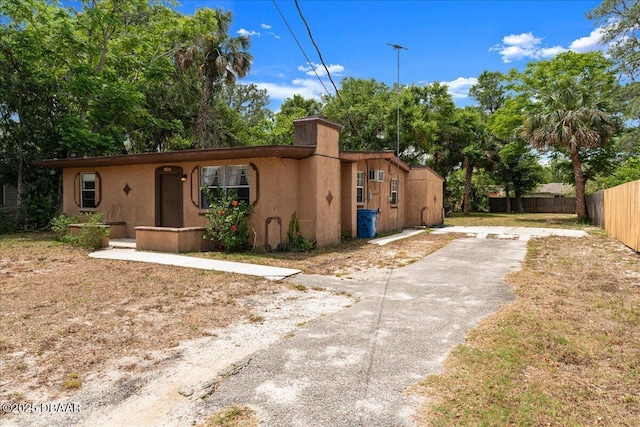 view of front facade featuring driveway, stucco siding, fence, and a chimney