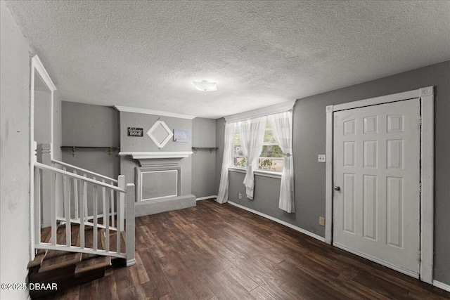 foyer with wood finished floors, a textured ceiling, a fireplace with raised hearth, baseboards, and stairway