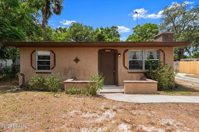 view of front of house featuring stucco siding, fence, and a chimney