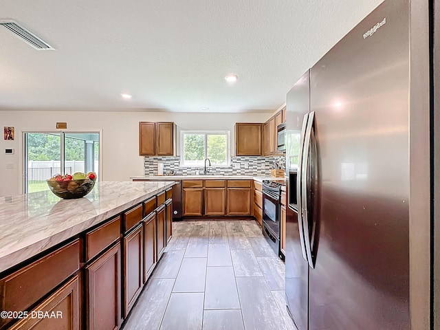 153 Orient Dr, Saint Augustine, FL 32092 - kitchen featuring appliances with stainless steel finishes, tasteful backsplash, light stone countertops, brown cabinetry, and recessed lighting
