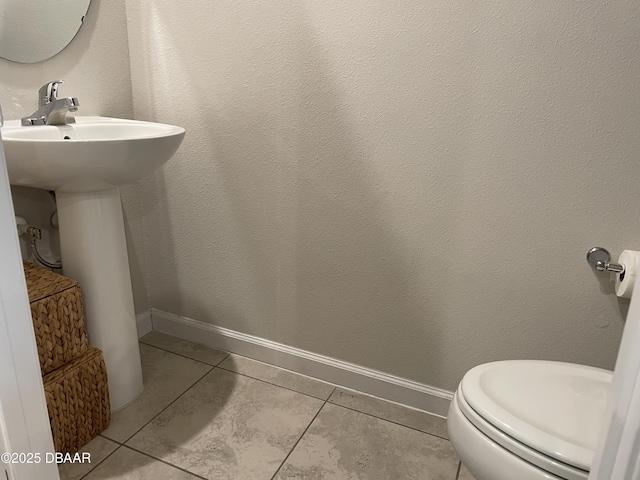 half bathroom featuring tile patterned flooring, baseboards, a sink, and toilet